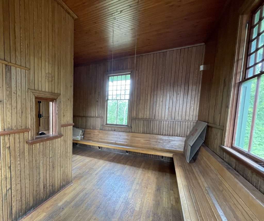 Freshly renovated interior of the historic Embrun train station, featuring restored wooden walls, benches, and ceiling with natural light streaming through large windows.